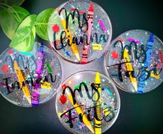 four clear glass coasters with colorful writing on them and green leaves in the background