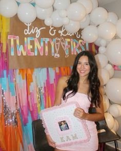 a woman in a pink dress is holding a cake and posing for the camera with balloons behind her