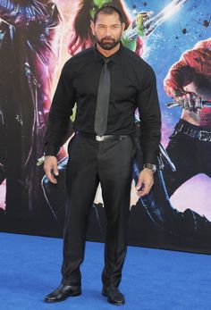 a man in a black shirt and tie standing on a blue carpet at the world premiere