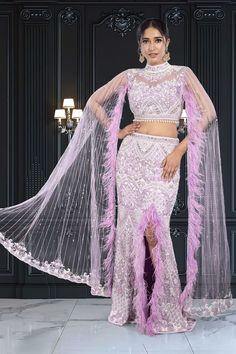 Get ready to turn heads with the Bridal Lehenga BL-299! This breathtaking outfit features a mermaid slit skirt adorned with stunning purple and white pearl and stone work. The high neck and cape feather sleeves add a touch of modern fun to your perfect sangeet night look. You'll feel confident and stylish all night long! Feather Sleeves, Sangeet Night, Purple Mermaid, Stone Work, Purple And White, A Mermaid, Night Looks