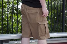 a man standing on a bench with his hands in his pockets and wearing brown shorts