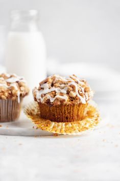 two muffins with icing and coconut on a plate next to a glass of milk