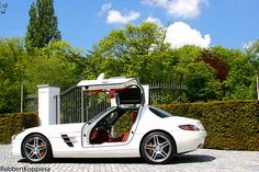 a white sports car parked in front of a gate with its doors open and the door opened