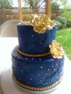 a three tiered blue cake with gold flowers on it's top and sides