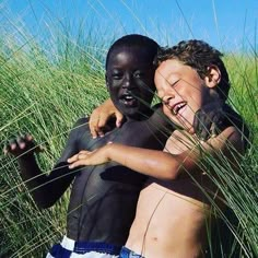 two young boys hugging each other in tall grass on a sunny day at the beach