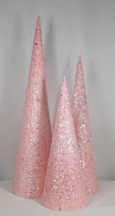 three pink glitter cone shaped trees on a white tableclothed surface, with one standing in the middle