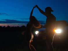 two people standing in front of a car with their hands up to the sky at night