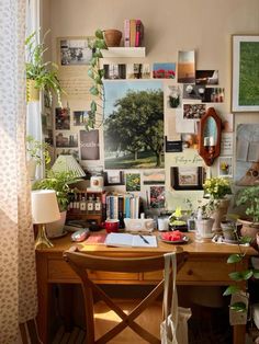 a wooden desk topped with lots of books and plants next to a wall covered in pictures