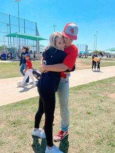 a man and woman hugging each other on a baseball field with people in the background