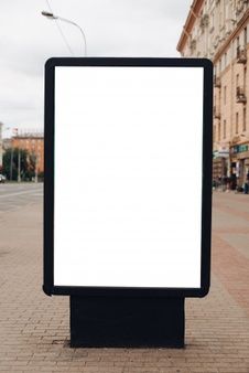 an empty billboard stands in the middle of a bricked street with buildings on both sides