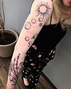 a woman with a sun and planets tattoo on her arm, standing next to a potted plant