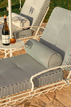 Striped outdoor chaise lounges with matching bolsters and a white side table, styled for luxury poolside comfort and wine enjoyment.