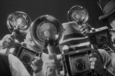 a group of men holding up some old cameras and looking at them in different directions