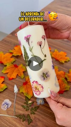 a person holding a candle with flowers on it and leaves scattered around the table in front of them