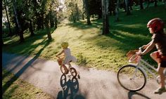 two children riding bikes on a path in the park, one is wearing a helmet and the other has a bicyclist