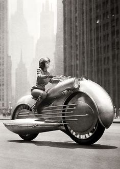 a woman riding on the back of a motorcycle in front of tall buildings and skyscrapers