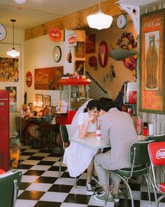 a man and woman sitting at a table in a room with coca - cola machines