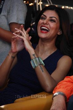 a woman sitting in a chair laughing and holding her hands together