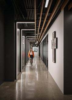 a woman walking down a long hallway in an office building with black and white walls