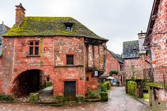 an old brick building with green moss growing on it's roof next to a cobblestone street