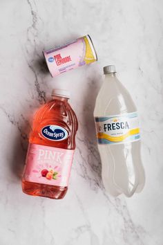 two bottles of water, one pink lemonade and the other orange juice on a marble countertop