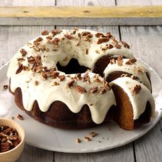 a bundt cake with white frosting and pecans on top sitting on a plate