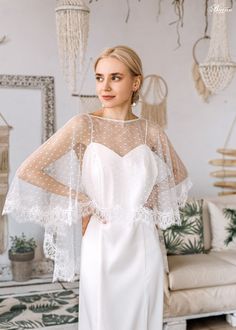 a woman standing in front of a couch wearing a white wedding dress with sheer sleeves