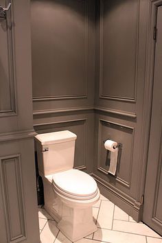 a white toilet sitting inside of a bathroom next to gray walls and cupboards on either side of it