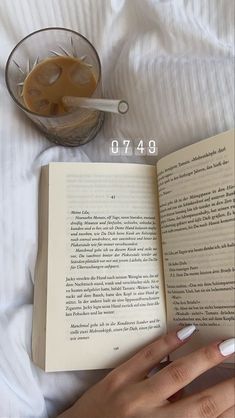 an open book sitting on top of a bed next to a glass filled with liquid