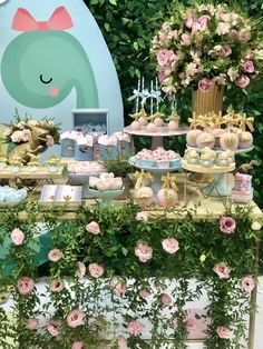 the dessert table is decorated with pink flowers and green foliage, along with cupcakes