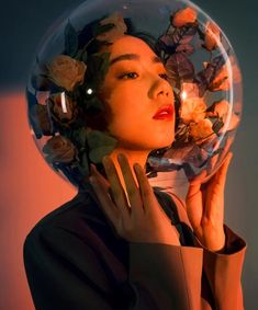 a woman with flowers on her head is holding a glass ball in front of her face