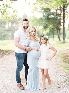 a pregnant woman and her husband pose for a photo with their daughter in the woods