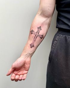 a person with a cross tattoo on their left arm and the other hand holding it