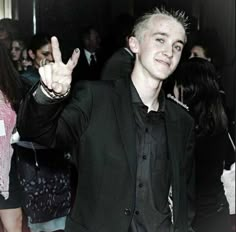 a young man in a suit and tie making the peace sign with his hand at a party