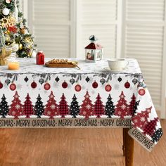 a christmas table cloth with trees and snowflakes on it, sitting in front of a small christmas tree