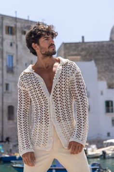 a man standing in front of some boats wearing a white knitted jacket and pants