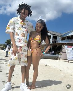 a man and woman in bathing suits standing on the beach, posing for a photo