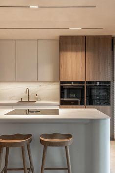 two stools sit in front of an island counter top and oven, which is built into the wall