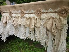 an old curtain with lace and flowers hanging from it's side in the grass