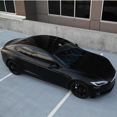 a black car parked in a parking lot next to a building with windows on it