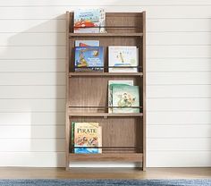 a book shelf with books on it in front of a white wall and blue rug