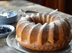 a bundt cake sitting on top of a glass plate next to bowls of blueberries