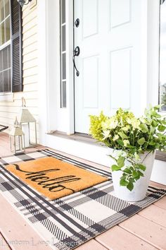 a potted plant is sitting on the front porch with a welcome mat and lantern