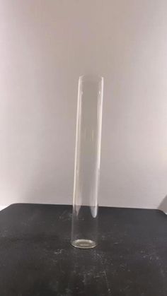 a tall clear vase sitting on top of a black table next to a white wall