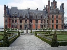 an old castle with hedges in front of it and a walkway leading to the entrance