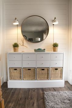 a white dresser with wicker baskets under a round mirror on the wall above it