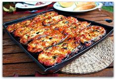 a pan filled with pizza sitting on top of a wooden table next to plates of food