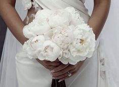 a bride holding a bouquet of white peonies in her hands and wearing a wedding dress