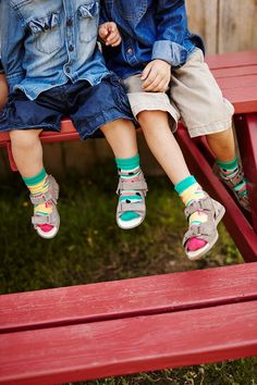 two children sitting on a red bench with their feet in the air and one child wearing green socks