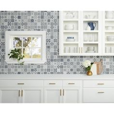 a kitchen with white cabinets and blue tiles on the wall, along with flowers in vases